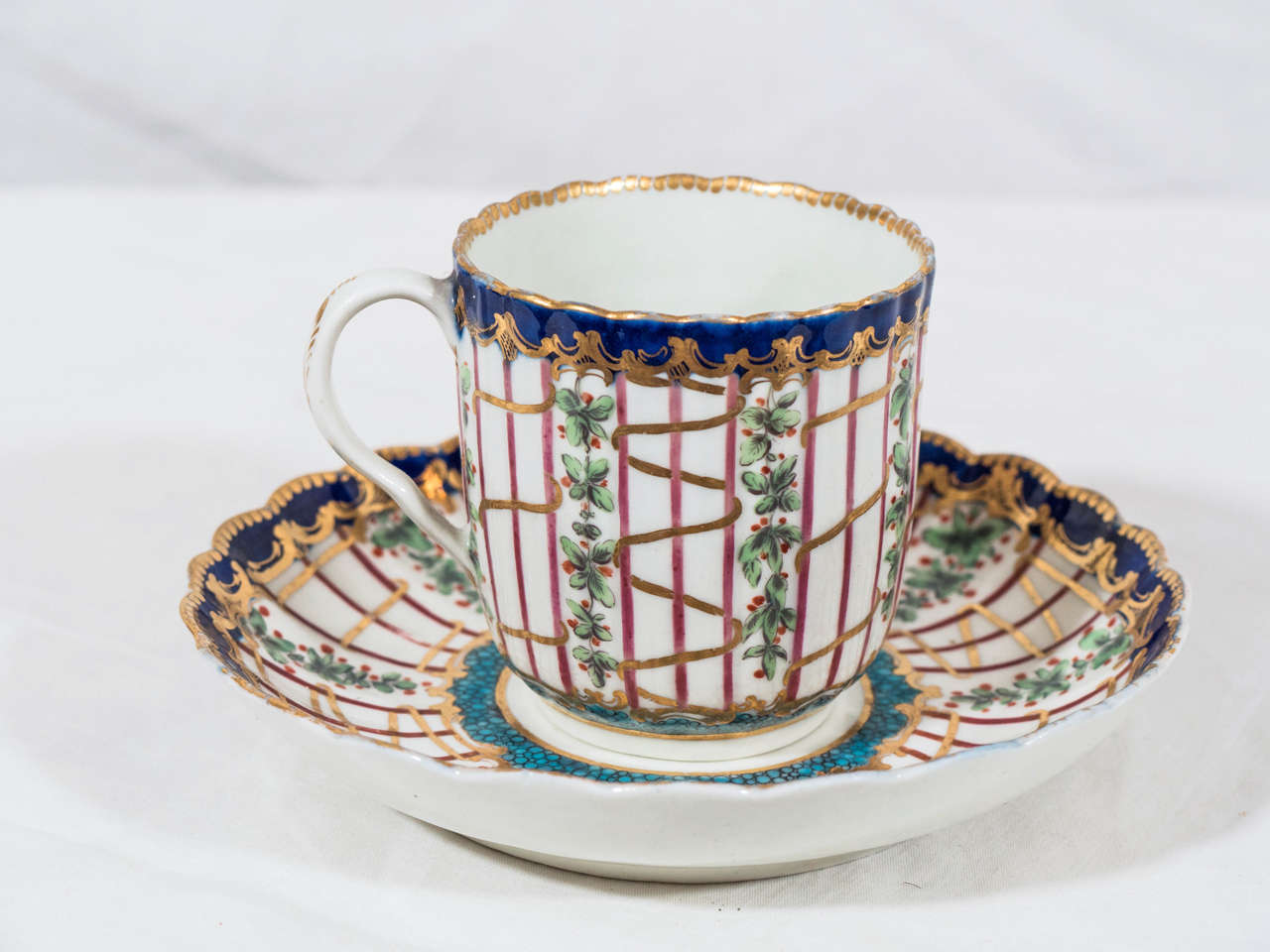 A very fine 18th century Dr. Wall Worcester soft-paste porcelain coffee can and saucer, fluted in the Sevres style with scalloped gilt edges. It is painted in over glaze colored enamels in a version of the 'Hop Trellis' pattern with a turquoise