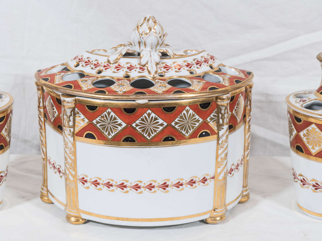 An exceptional three piece Chamberlain Worcester mantel garniture consisting of a bough pot and a pair of root pots painted with a neoclassical design. Contrasting gilded diamonds and black semi-circles decorate an iron red ground.
For an image of