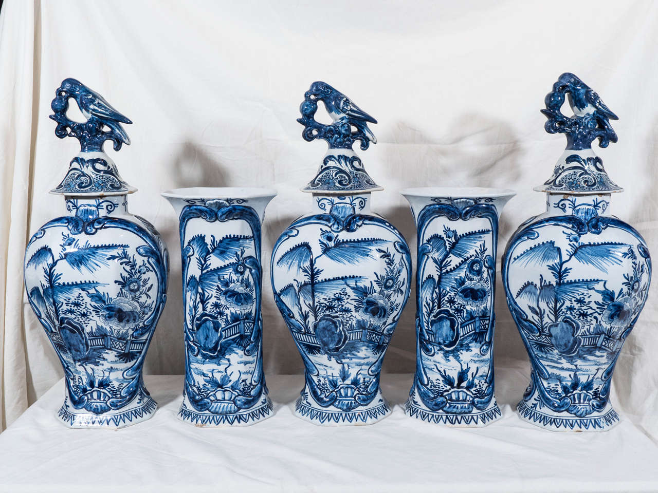 A Dutch five-piece garnitures decorated in cobalt with a lovely garden scene showing a flowering tree, a large peony, and a garden fence. The three covers have traditional bird and ball finials. The reverse of each vase is decorated with an