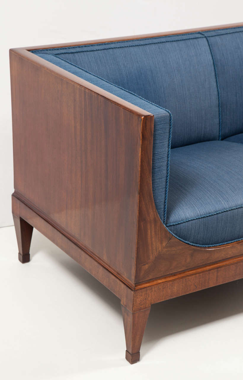 A classic Frits Henningsen rich mahogany and upholstered sofa, Circa 1930s, the rectangular backrest and sides upholstered in panel style, the front frieze with graceful curved ends, above a recessed plinth base raised on square tapered legs ending