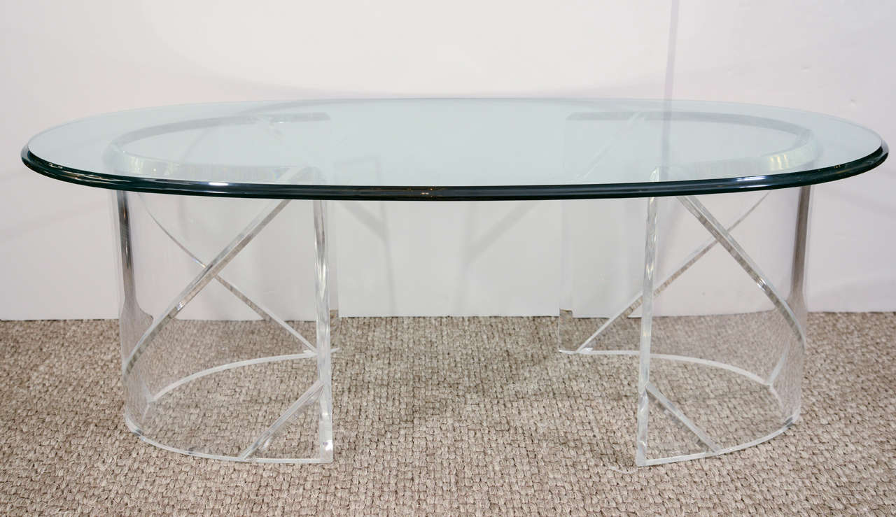A chic and sleek coffee table with two semi-circle lucite pedestals and an oval glass top.