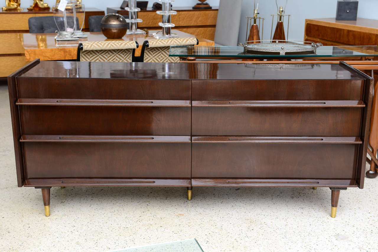 The rectangular top above six conforming drawers with full length pulls and cutouts on round tapering legs ending in brass caps.
