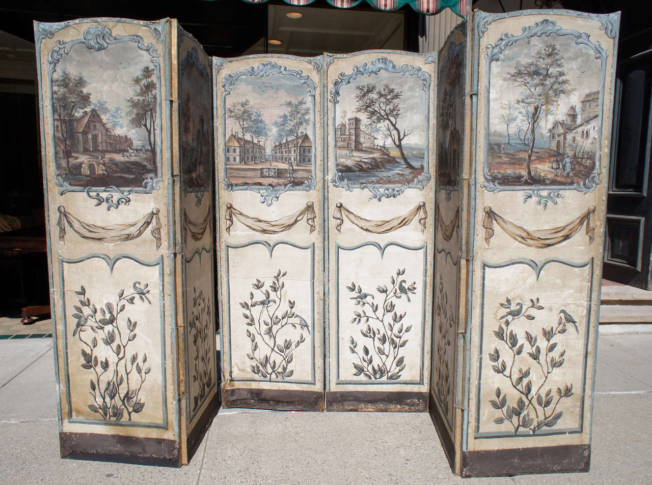 This lovely and unusually large 6 panel French screen is painted in a late 18th century style and manner. The scenes depicting various buildings , people and bucolic settings are further enhanced with  draped swags and floral specimens. These are