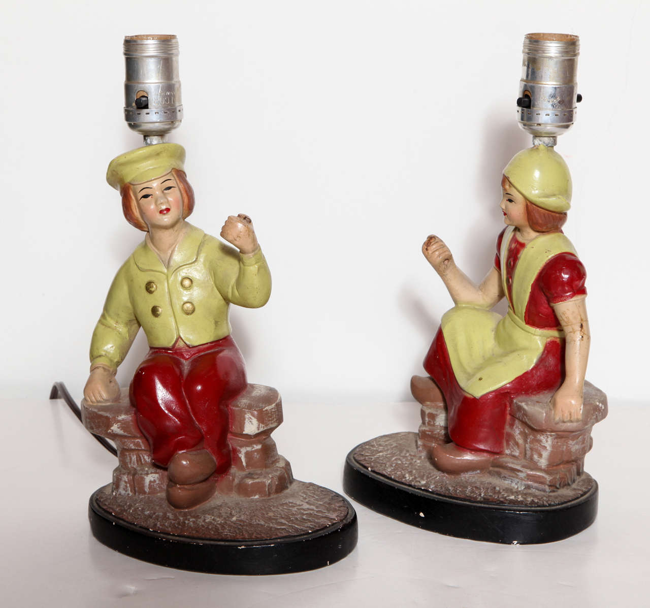 A pair of painted plaster American Folk Art vanity lamps. One is styled to look like a Dutch boy and the other a Dutch girl--both in traditional dress. Lamps take clip-on shades. Wired and working. Stamped Colonial Art Creations.