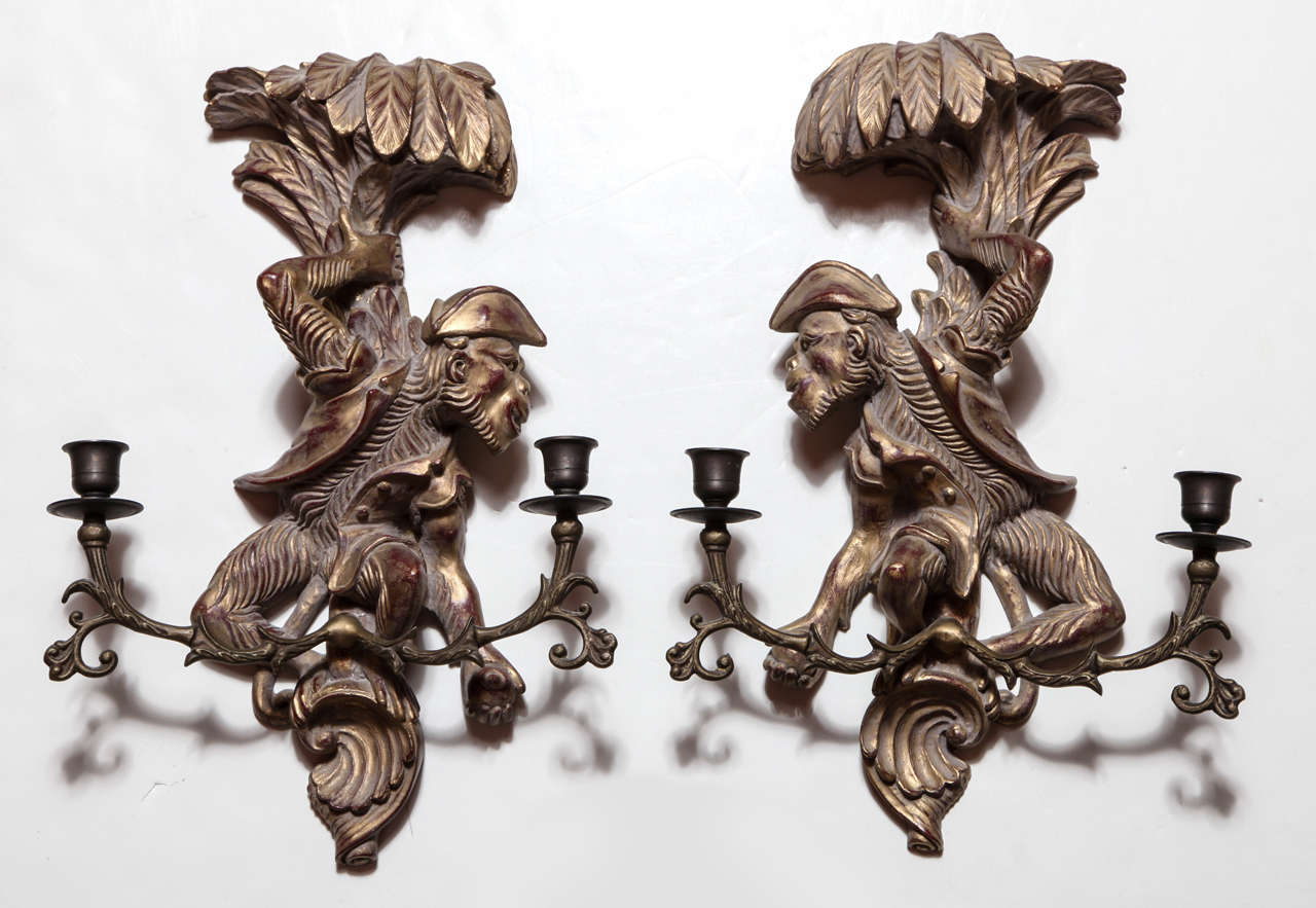 A pair of mid-20th Century Rococo-style gold-painted wooden monkey sconces. Each sconce can support two tapper candles.