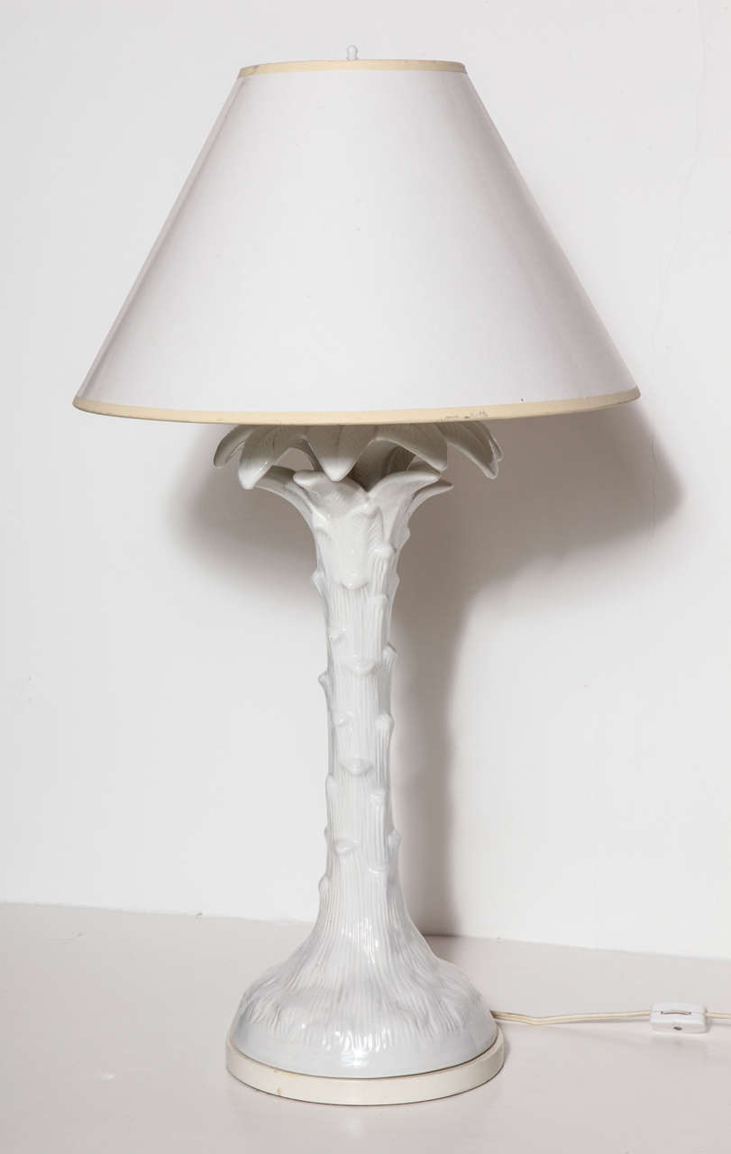 A 1970's white glazed ceramic palm-styled lamp in the manner of Serge Roche. The lamp features a double bulb socket and a white lacquered shade. Wired and working.