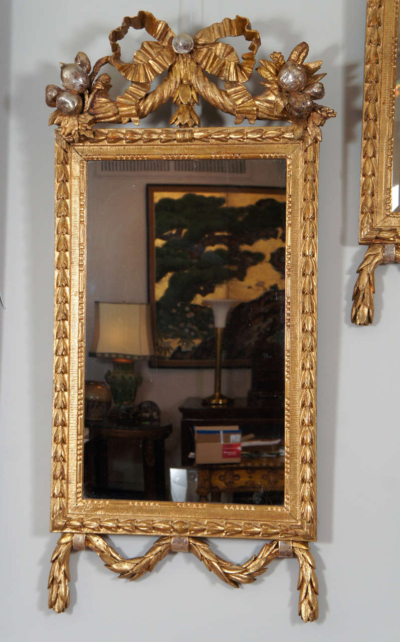 Beautiful pair of gilt mirrors with carved bow, cornucopia and garland details.
One mirror has original mirror glass and the other was replaced later with a bevel.
