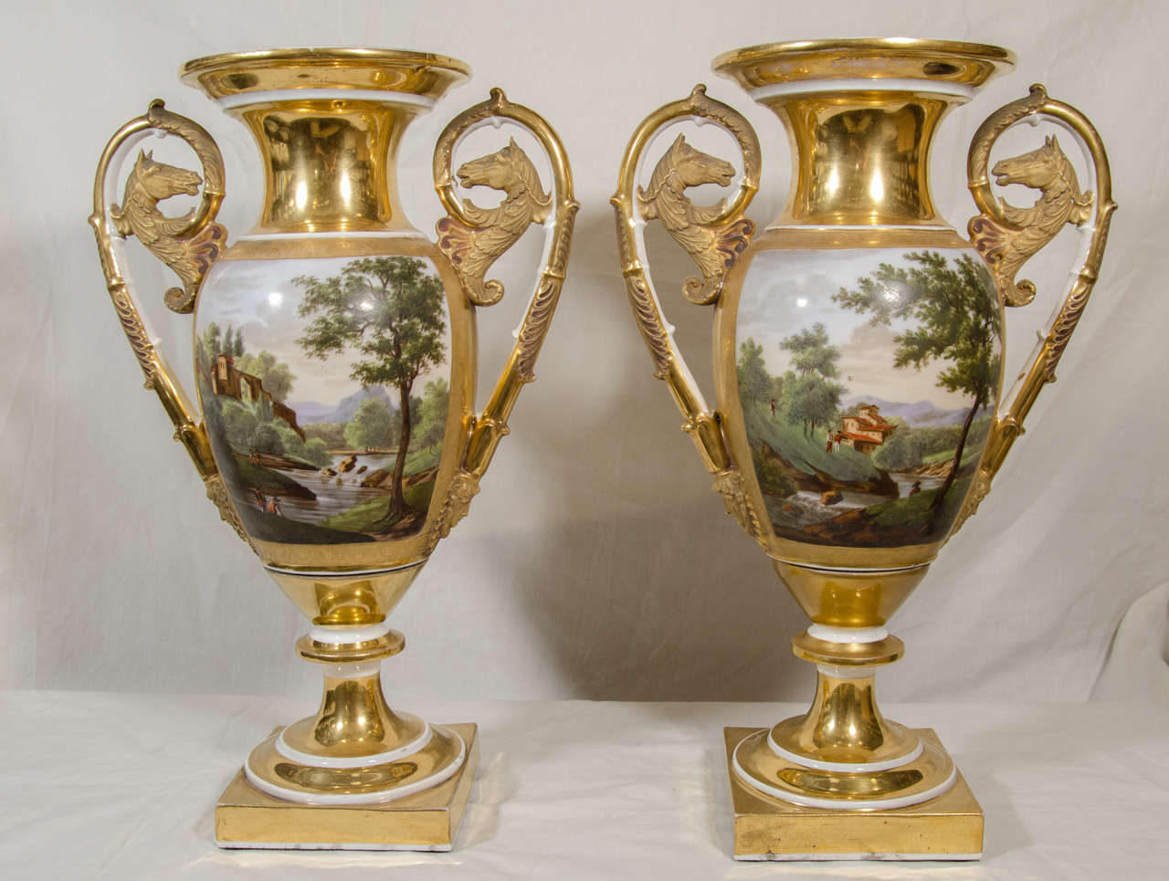 A pair of gold ground porcelain vases painted with rustic figures in rural landscapes. The matte gilding of the handles emphasizes the painted reliefs. The quality of the painting and gilt decoration are characteristic of the style of the Nast