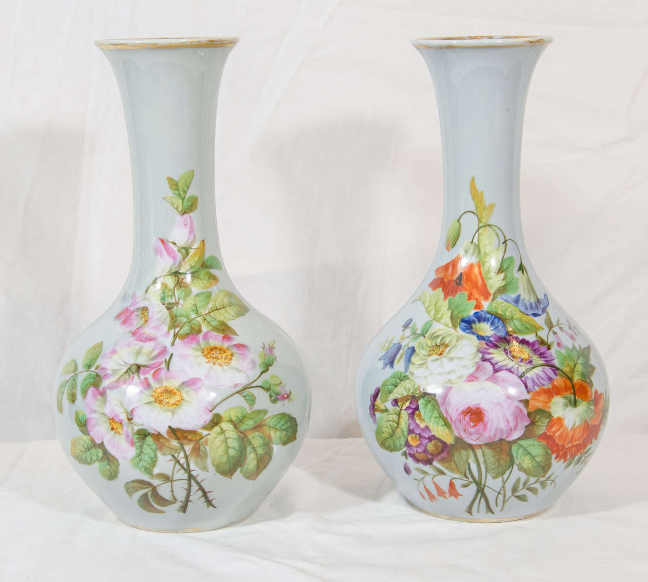 This lovely pair of 19th-century opaline vases have well-painted flowers. Individually hand-painted, each with a bouquet of peonies, tulips, and other flowers on a light blue ground. 
The glass is slightly translucent, as opaline should