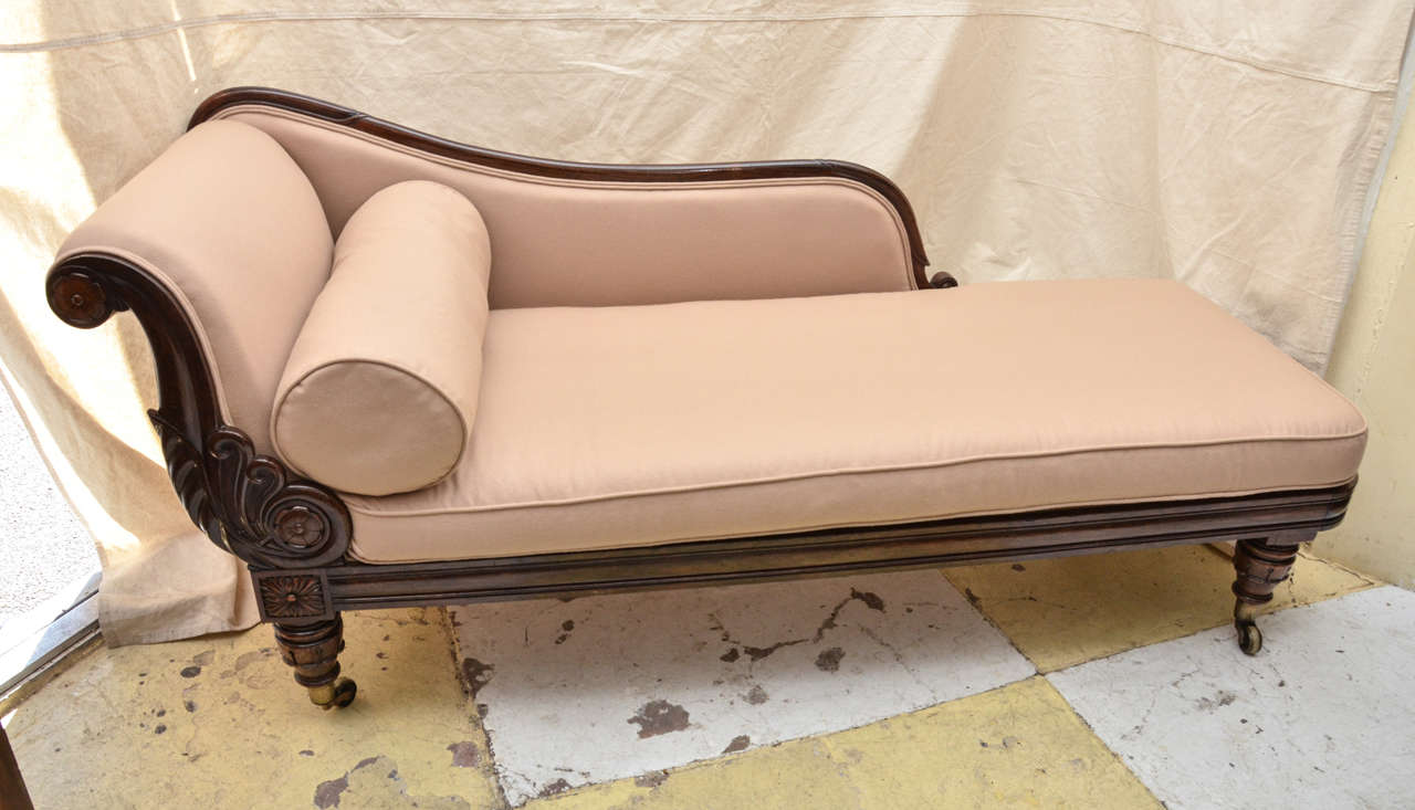 English Rosewood framed William IV recamier / chaise lounge. The chaise has a boldly carved Neoclassical influenced floral scroll arm support. Terminating in a rosette at the top and bottom. Their are 4 lappet carved short legs on brass cup castors.