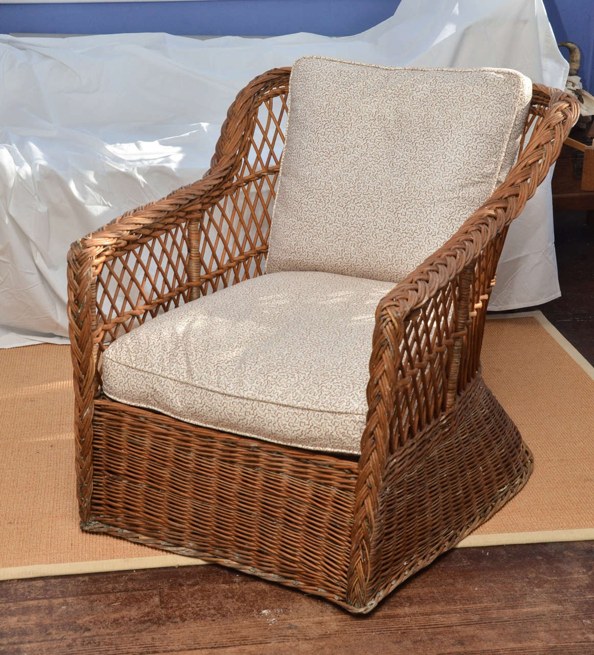 A large-scale American 1920's natural wicker feather cushioned lounge chair. The arms are topped with a braided pattern, the back and sides are woven in a lattice pattern, the feather cushions are covered in a 1980s brown and cream coral pattern.