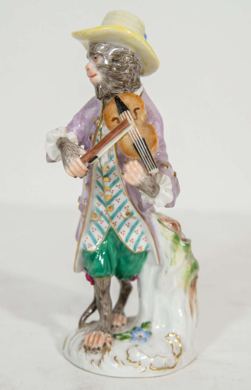 A FIne Meissen Porcelain Monkey Musician Figurine of superb quality. This unusual Monkey figurine is playing the Obo musical instrument dressed in a well detailed hand enameled gilded purple jacket with yellow enameled pants and multi color feathers