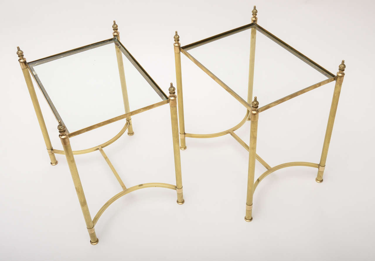 1960s pair of Bagues-style brass and glass side tables with reeded column, flame finials, inverted bow cross stretchers and clear glass tops.