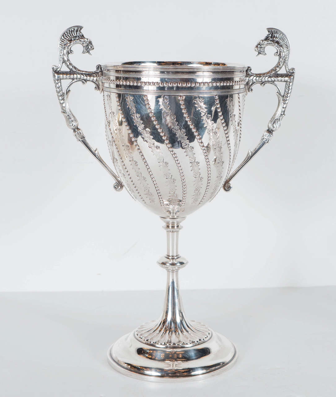 This elegant Hollywood Regency silver plated chalice features intricate floral and beaded detailing, sculptural dragon gargoyles on the handles, as well as a fluted cascading base. A great decorative item for a bookcase or display or really gorgeous