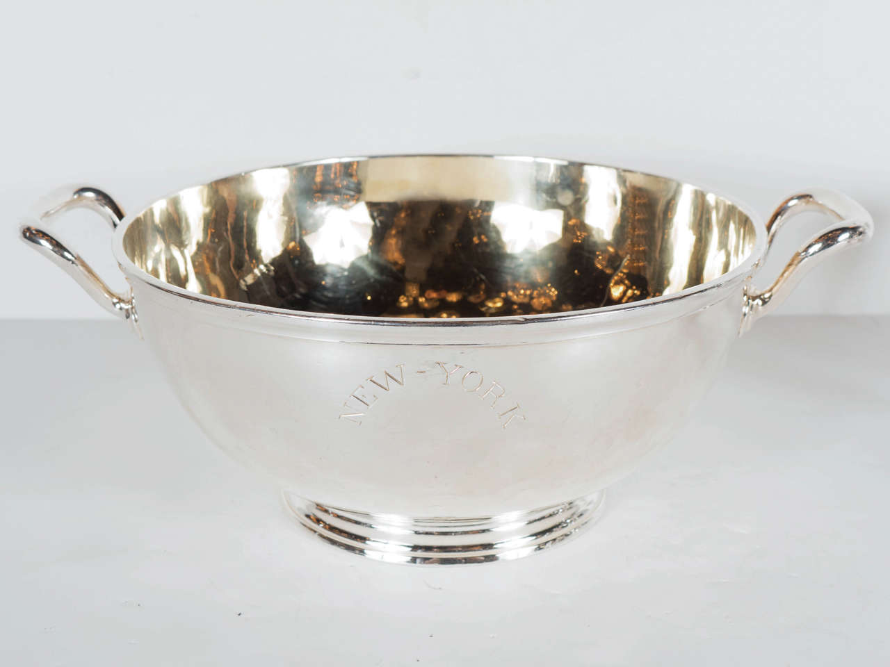 This stunning bowl is made of fine silver plate with a gilt interior. It features a two arm form with a concentric stepped base. It has an engraving on the front 