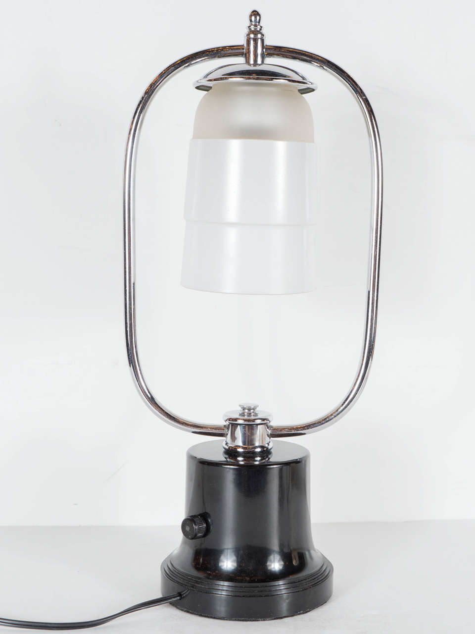 This exceptional Art Deco Machine Age table lamp is superb. Created in the manner of Walter Von Nessen it features a bakelite base with a chrome arm form design suspending a stepped skyscraper form globe in milk and frosted glass. This lamp would be
