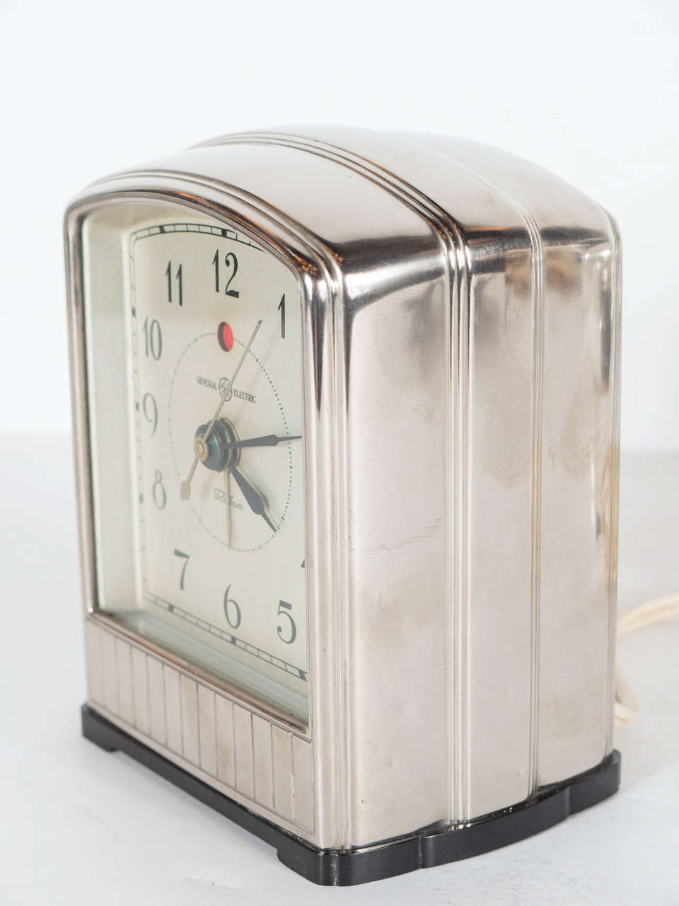 This exceptional streamlined Art Deco electric desk clock is by Telechron. It features a square chrome design with streamlined incised lineal fluted detailing. It rests on a skyscraper style black bakelite base. This clock has a built in light and