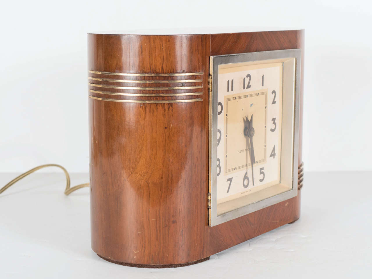 This exceptional Art Deco clock by Seth Thomas features a streamlined design with rounded ends decorated with a lineal brass inlay detailing at each end. The clock strikes on the hour (this feature can be disabled) and is electric. The case is all