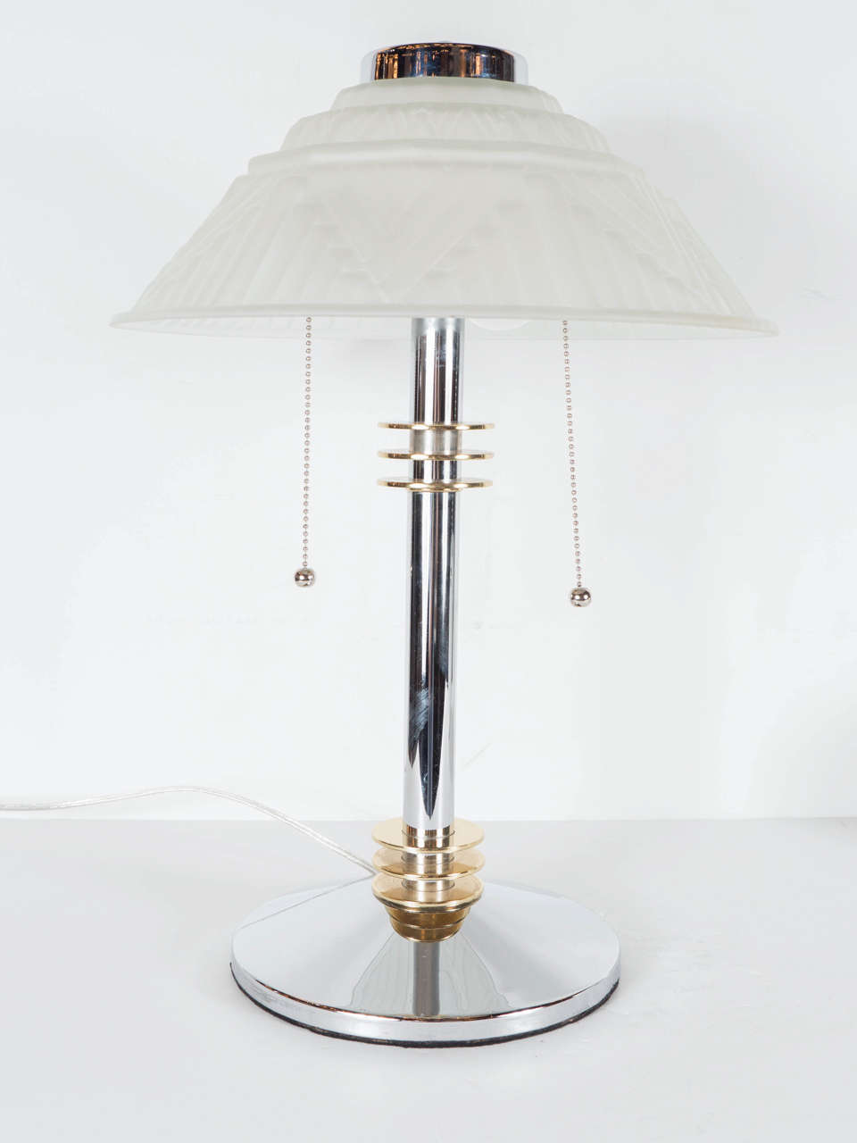 This stunning Art Deco skyscraper style table or desk lamp is beautiful and exceptional. It features relief frosted glass globe shade with a stylized Art Deco geometric design, a chromed base and neck, with circular accents of brass. It is in