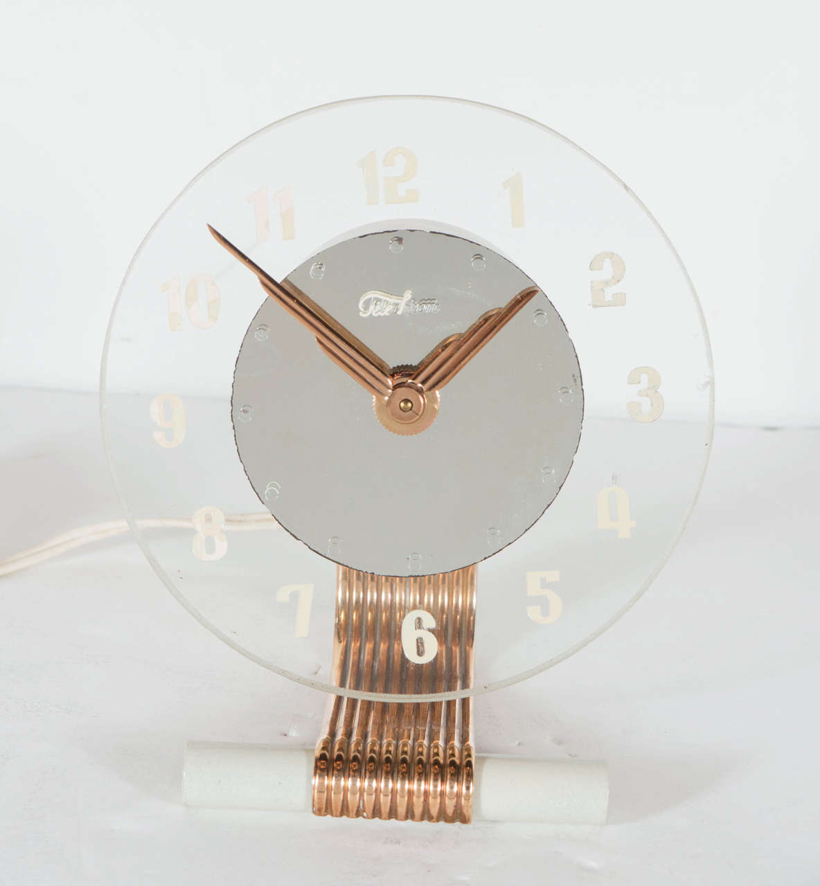 This sculptural Art Deco Modernist electric desk clock by Telechron features a cantilever design, a ribbed brass band that wraps around an ivory enamel stem and bends back on itself to support the clock casing. It has a circular clear glass face