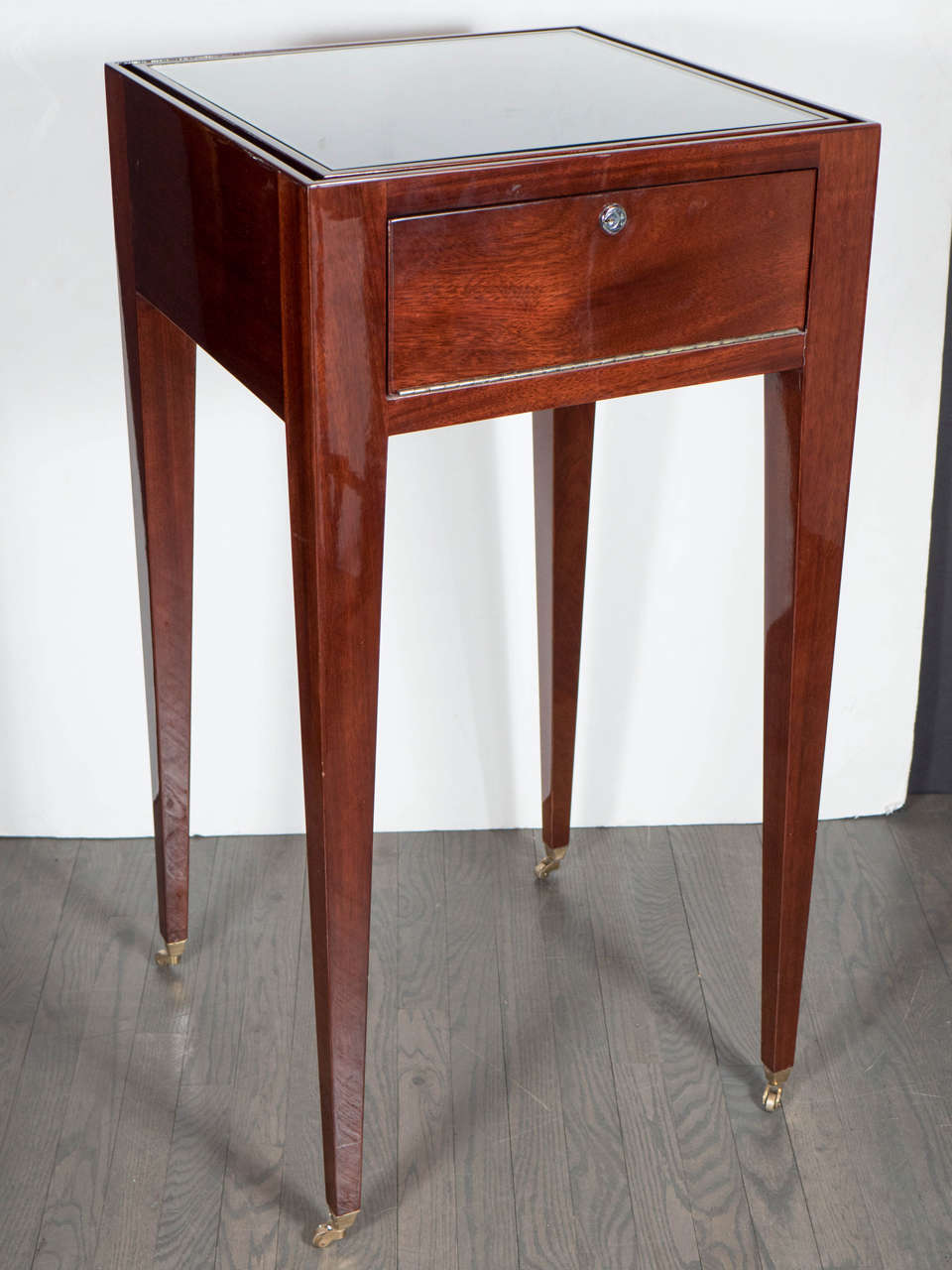 This elegant Art Deco Directoire style display case was realized in France, circa 1930. It features a rectilinear body with tapered legs in fine Mahogany sitting on brass castors. Additionally, it offers one pull out drawer, which is lockable and