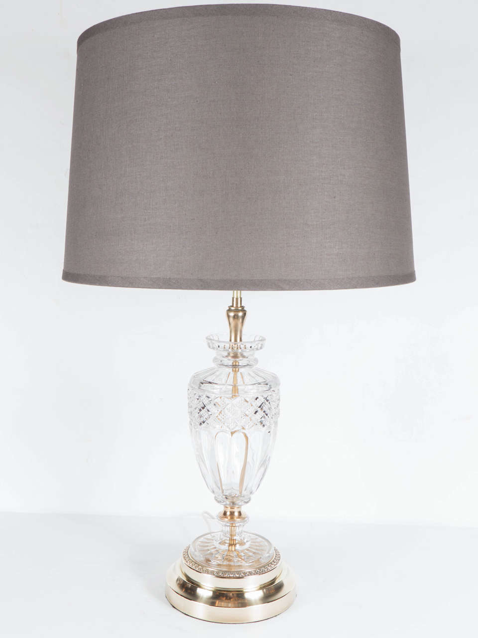 This elegant pair of Hollywood Style table lamps feature crystal urn style bases with fluted, starburst and cross-hatch detailing mounted on stepped brass footings. Each lamp has two bulbs (max 75 watts per bulb) with pull chain switches which can