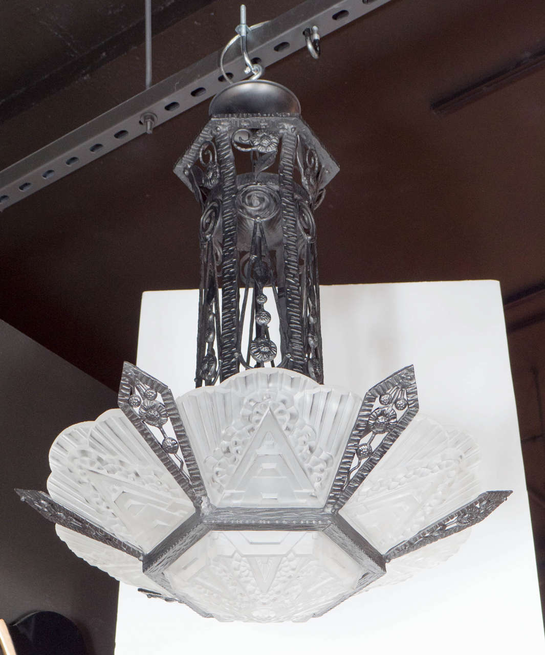 This stunning chandelier features exceptional relief frosted glass with highly stylized Art Deco geometric detailing. The frame of the chandelier is hand wrought black iron. with stylized floral,foliage and lineal detailing. It has been completely