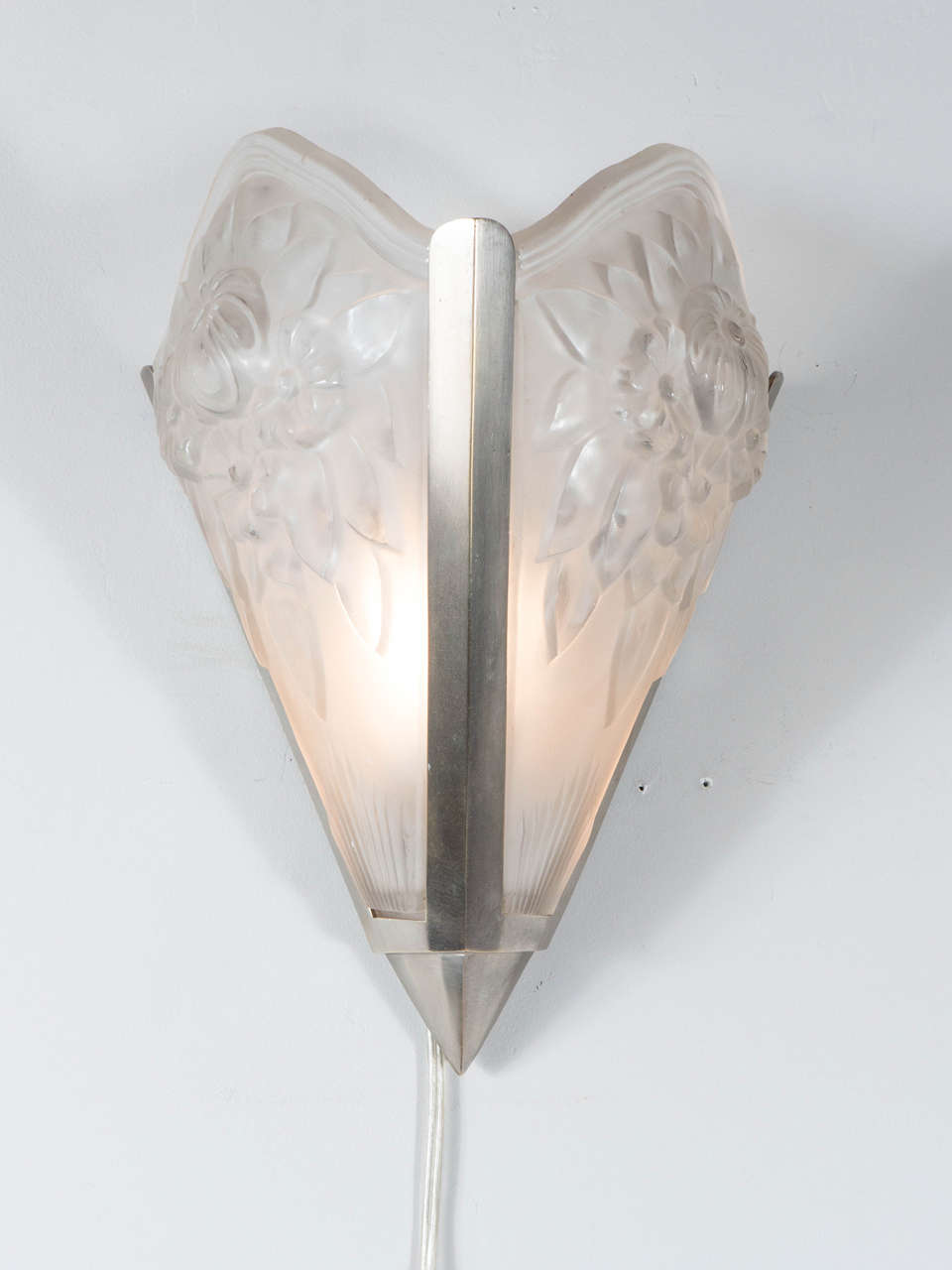 This sophisticated Art Deco sconce is in the manner of Degue. It features two panels of relief frosted glass with a bouquet  of floral detailing mounted in a brushed nickel frame. It has been newly rewired.