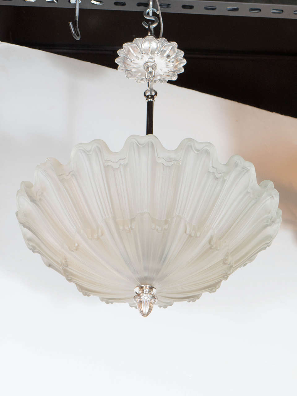 This exquisite Art Deco chandelier in the manner of Lalique features a frosted glass bowl with scalloped detailing which repeats on itself at alternating heights, the nickel canopy and finial are original and feature laurel detailing which extends