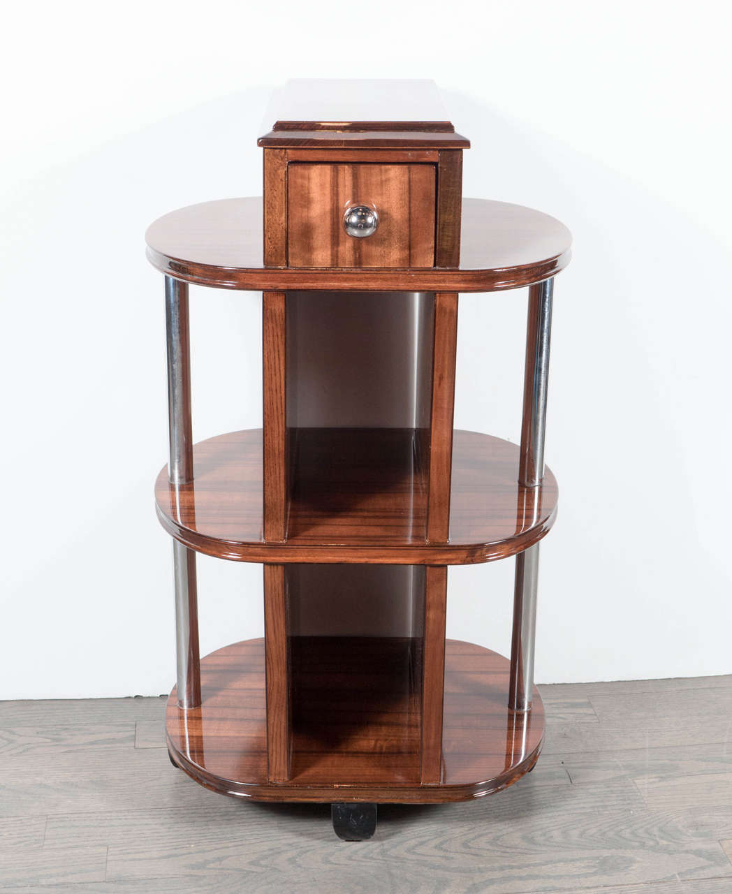 This versatile Art Deco Machine Age side table features a streamlined multi-tiered design in book-matched walnut, a drawer with a chrome pull and parallel chrome rods that run through the shelves. This is a great example of the Machine Ages