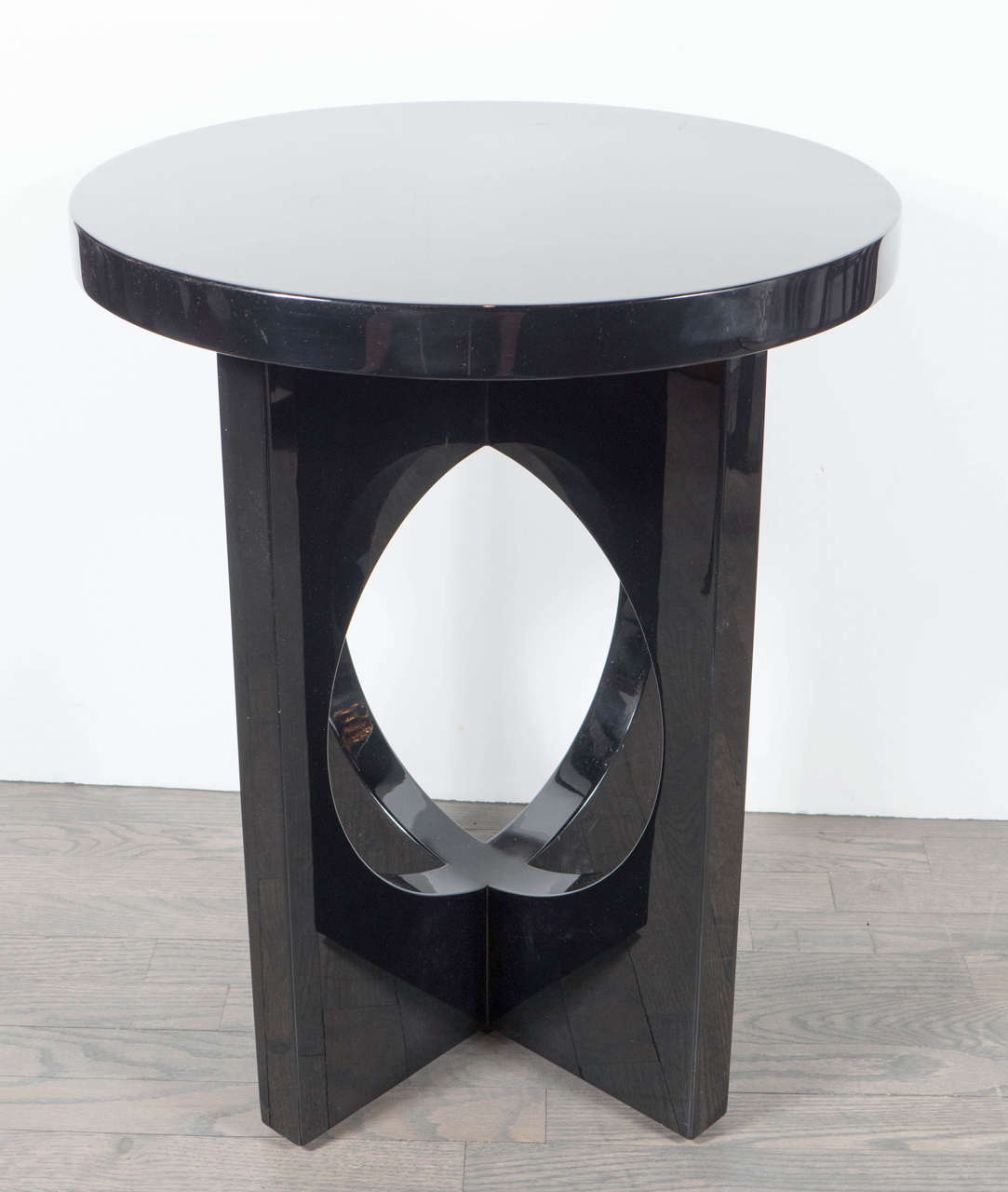 Pair of Mid-Century Modernist round occasional tables in black lacquer with intersecting criss-cross supports accentuated with stylized geometric cut-out designs. This sleek pair of Mid-Century Modernist tables feature thick rounded table tops that