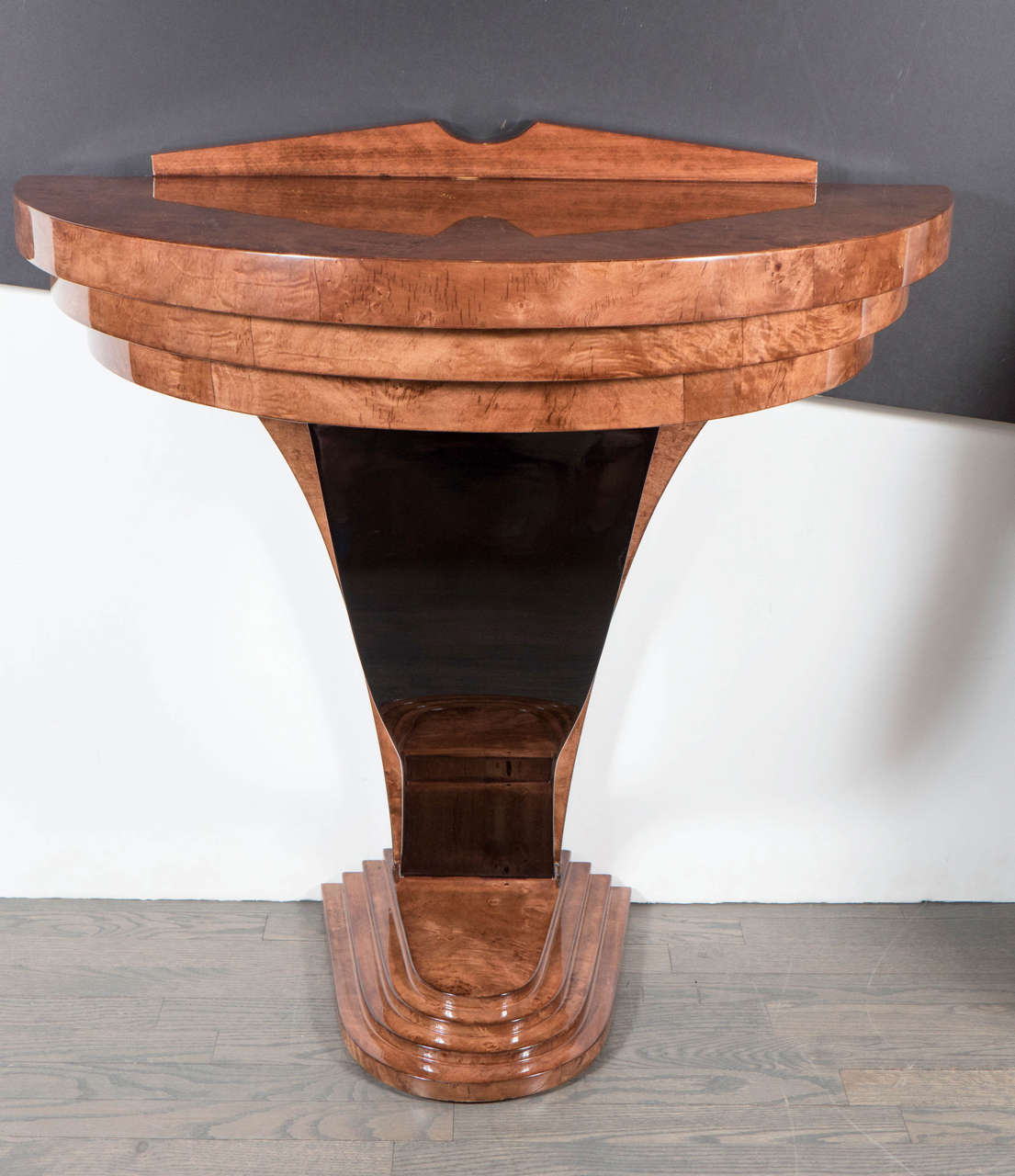 This stunning Machine Age Art Deco console was realized in the United States, circa 1935. Executed in bookmatched carpathian elm, it offers a demilune form skyscraper style base consisting of four stepped tiers from which a streamlined black lacquer
