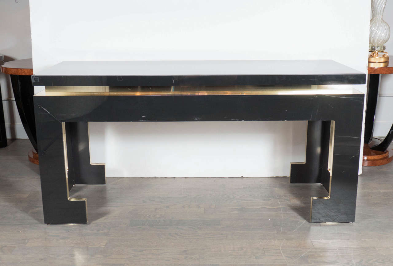 This stunning Mid-Century Modernist console with Greek key styling features a sleek stylized overall design with its ultra-thick base supports and a multi-dimensional feel with its brass banding that outlines the interior of each vitrioled plane.