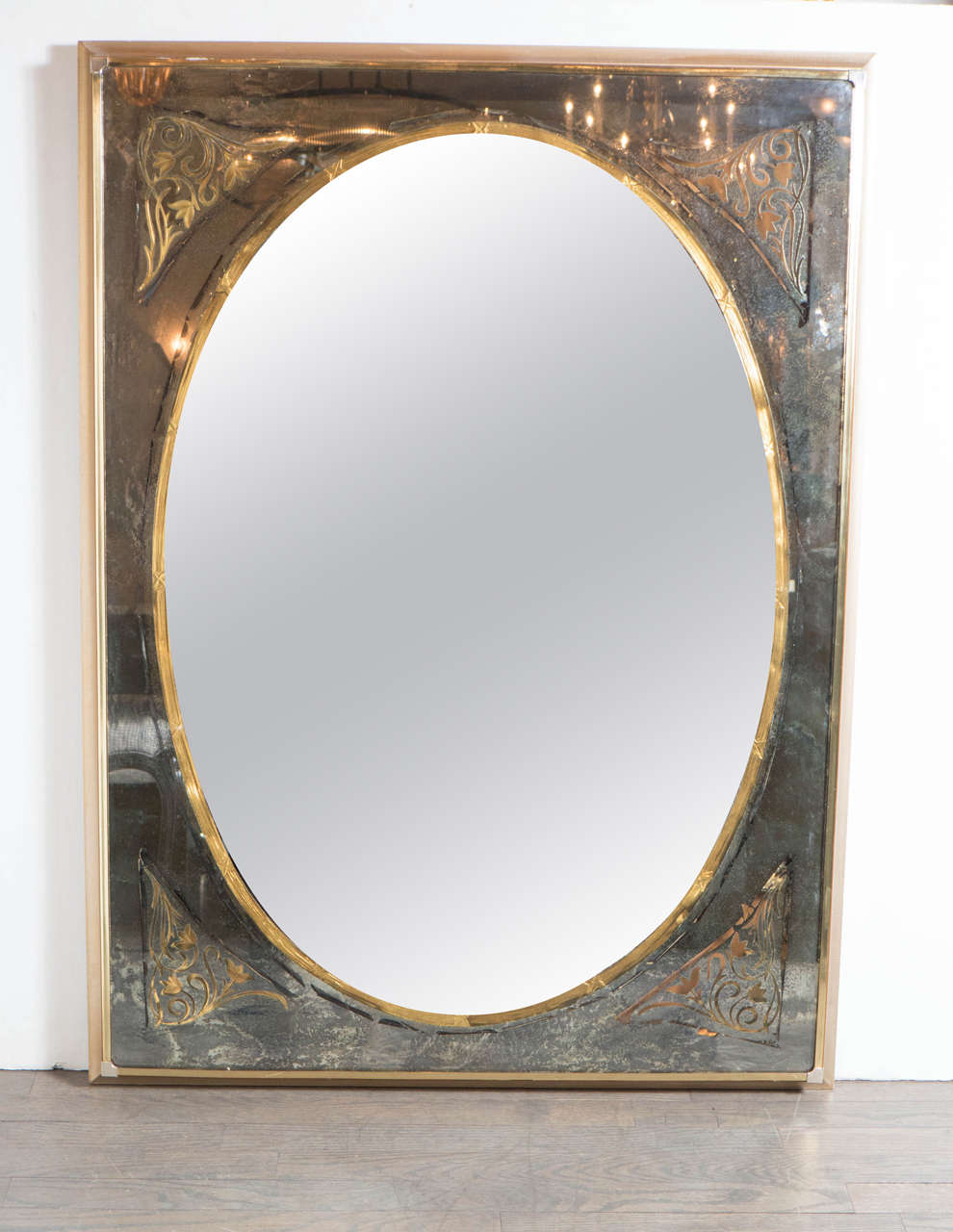 This elegant Mid-Century Modernist mirror in the manner of Jansen features reverse eglomise stylized floral and scroll detailing in each corner, a clear oval mirror center with gilt surround with 