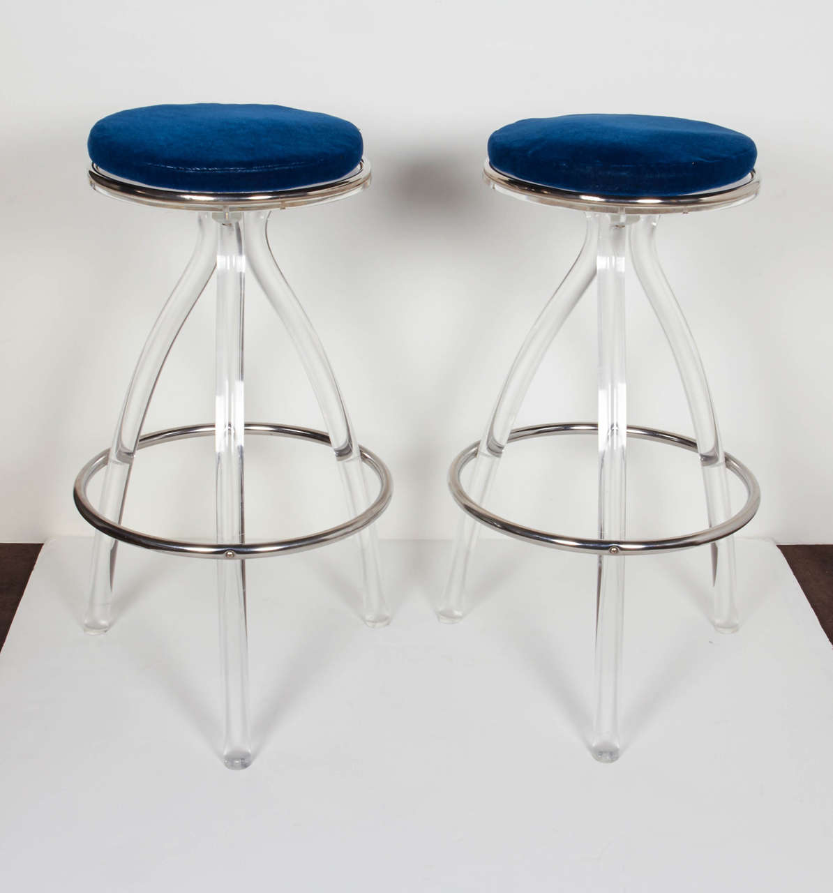Pair of Mid-Century Modern bar stools in Lucite. The stools have circular seats with chromed banded details. The stools have elegant scrolled bases with tripod leg design and also feature circular chrome footrests. They work as counter stools and
