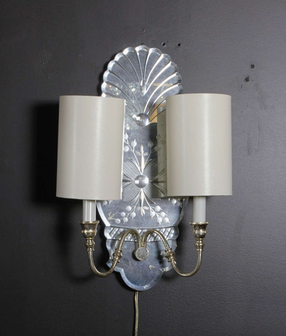 These elegant sconces are designed with a beautiful scalloped form. Intricate reverse etching design throughout, including hand beveled borders. Additional gold fleck details and S-shaped nickeled arms. Includes four custom ivory shades with tall