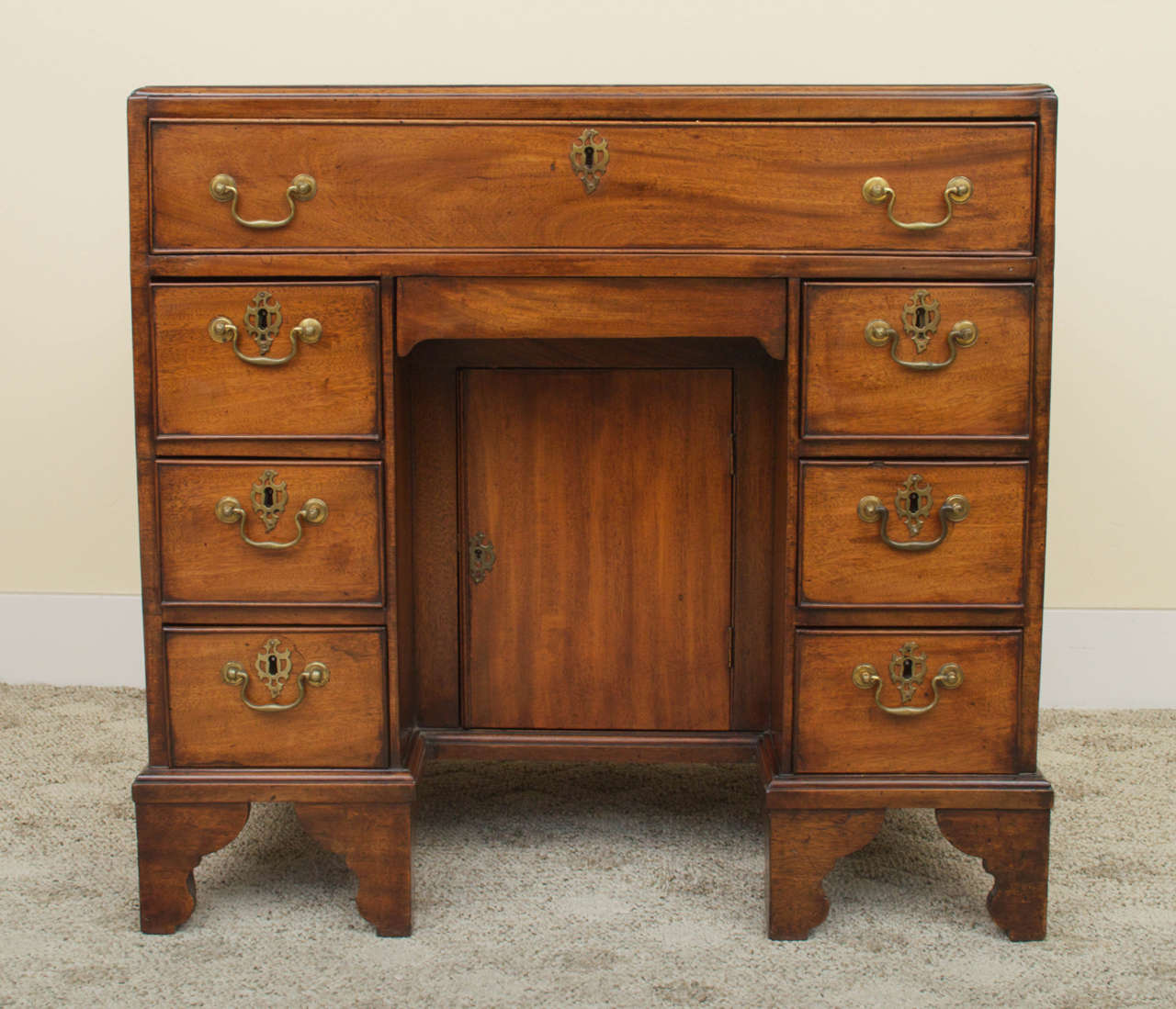 A stunning English, George II, solid mahogany kneehole desk. The crossbanded top is slightly warped due to age. There is one large beaded frieze drawer above a kneehole drawer and recessed cupboard that is flanked by six small beaded drawers. Both