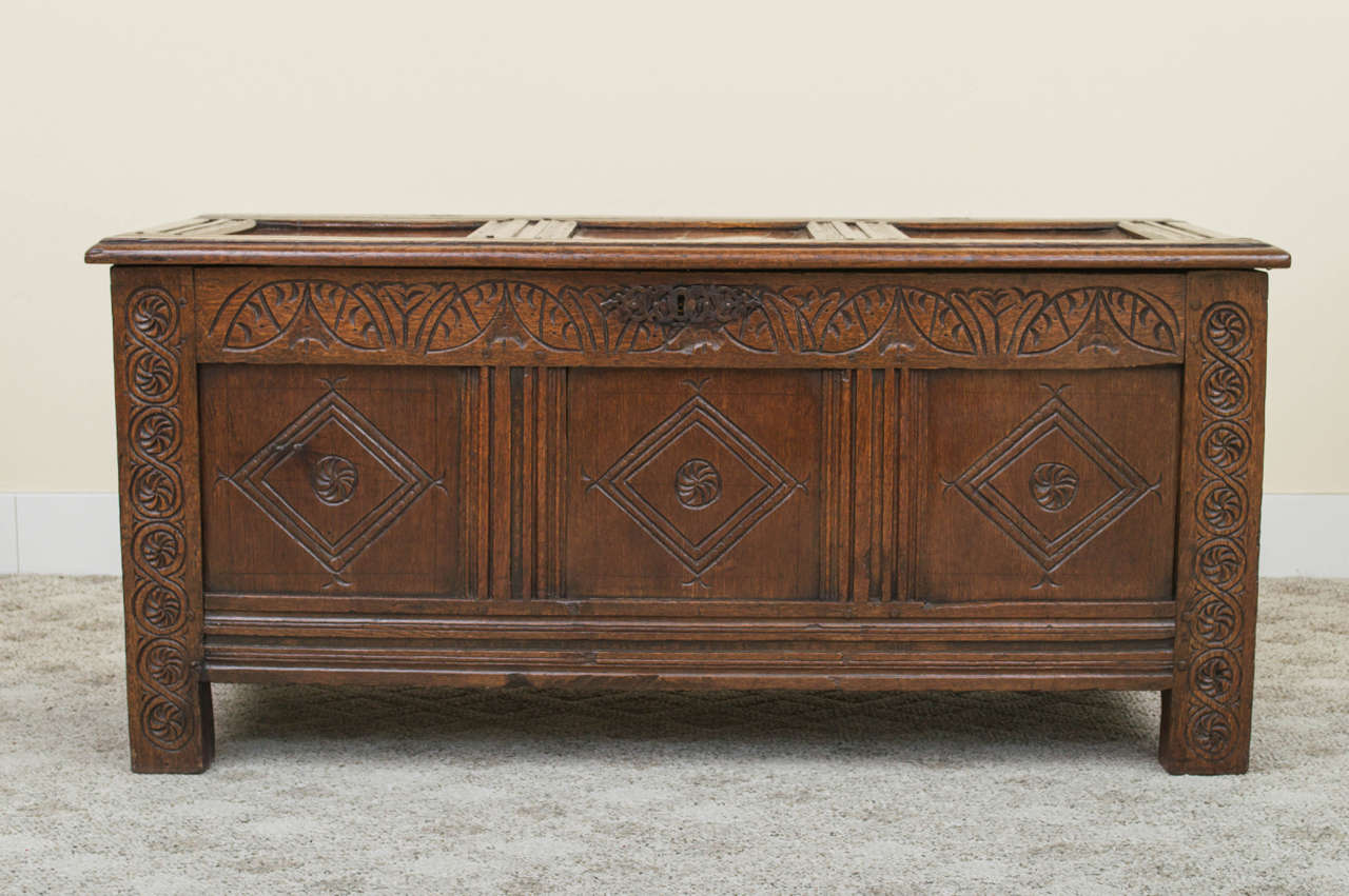 A magnificent English William and Mary carved solid oak coffer. The three-panel front is hand-carved with florets centered in diamonds and has carved scroll pilasters going up and down both sides. The lid and sides are also paneled. The interior is