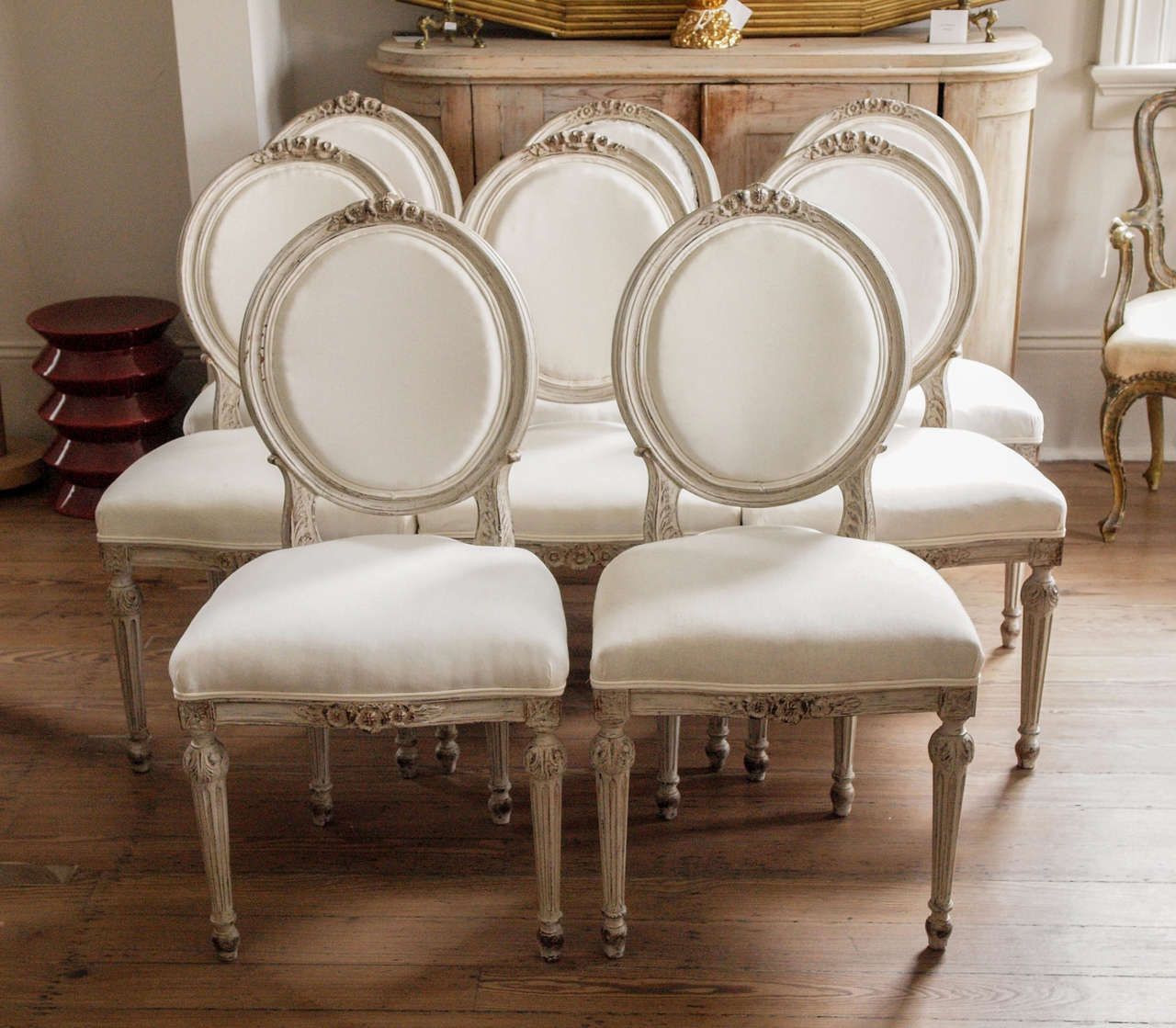 8 very comfortable Gustavian dining chairs newly upholstered in muslin.  Carving on front rail and back, fluted legs.  Pale grey paint.