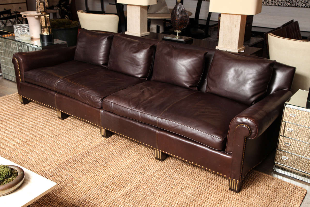 A beautiful chocolate brown leather sofa covered in the softest buttery Cabretta leather with brass nail heads and gilt wood details on the fluted feet. The sofa has paneled arms that also have a brass nail head detail. The seat cushion is divided