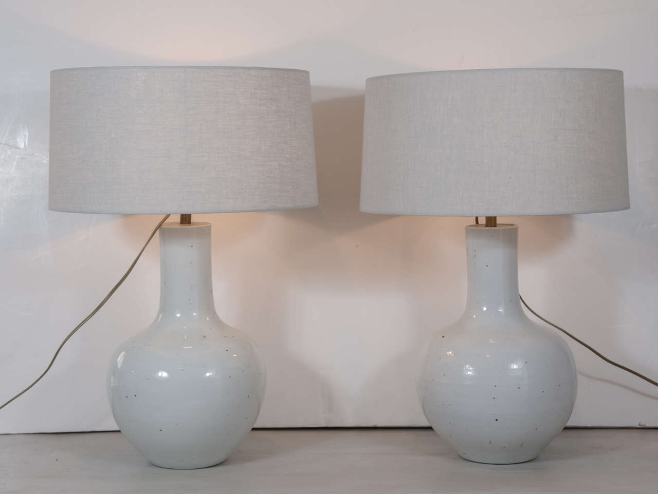 Pair of vintage long neck white vases, newly wired as table lamps with rolled-edge shallow drum shape linen shades.