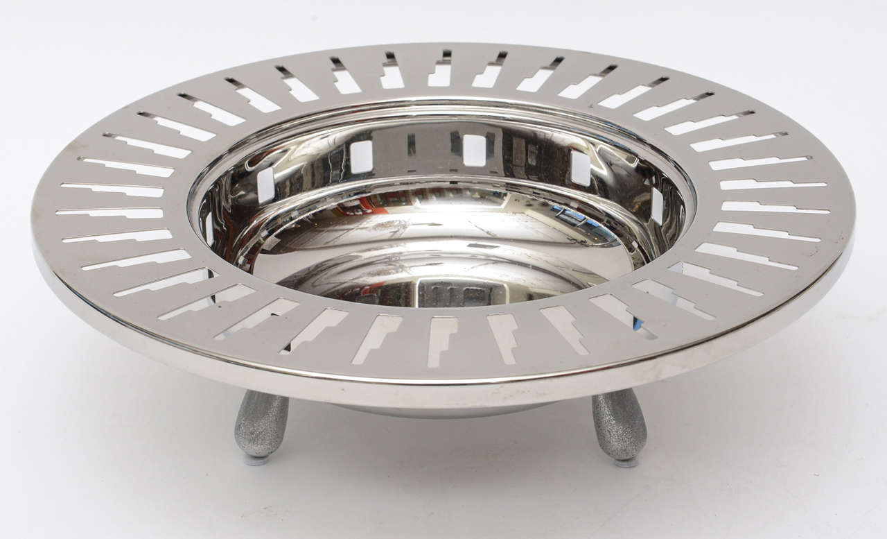 This lovely Italian Alessi stainless steel 3 footed cutout bowl is of deco inspired partial skyscrapers buildings in more of an abstract form. This is a discontinued bowl and is most likely from the 1990s. We have not professionally polished