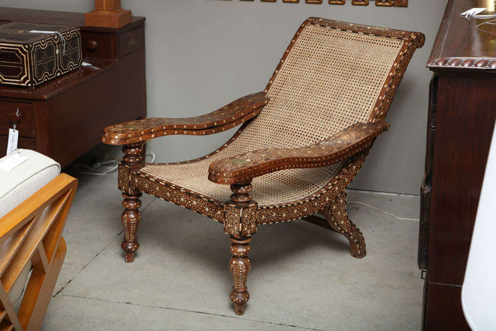 A rare pair of capacious antique rosewood plantation armchairs from Mussorrie, Northern India, with allover bone inlay, the frame banded with ebony and bone, the two swing out armrests attached by a brass medallion with newly caned seats.  The back