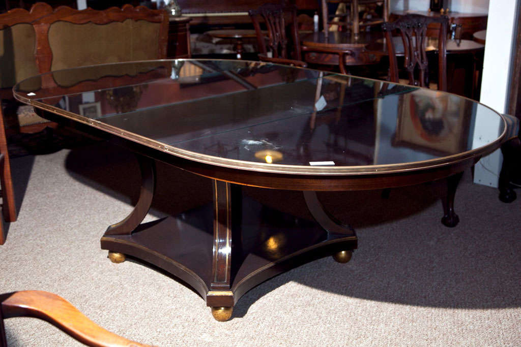 A fine mahogany Maison Jansen circular dining-room table. The gilt bun feet supporting a concave gilt framed undercarriage leading to a group of framed gilt gold concave legs. The solid mahogany tabletop having a solid bronze border encasing a glass