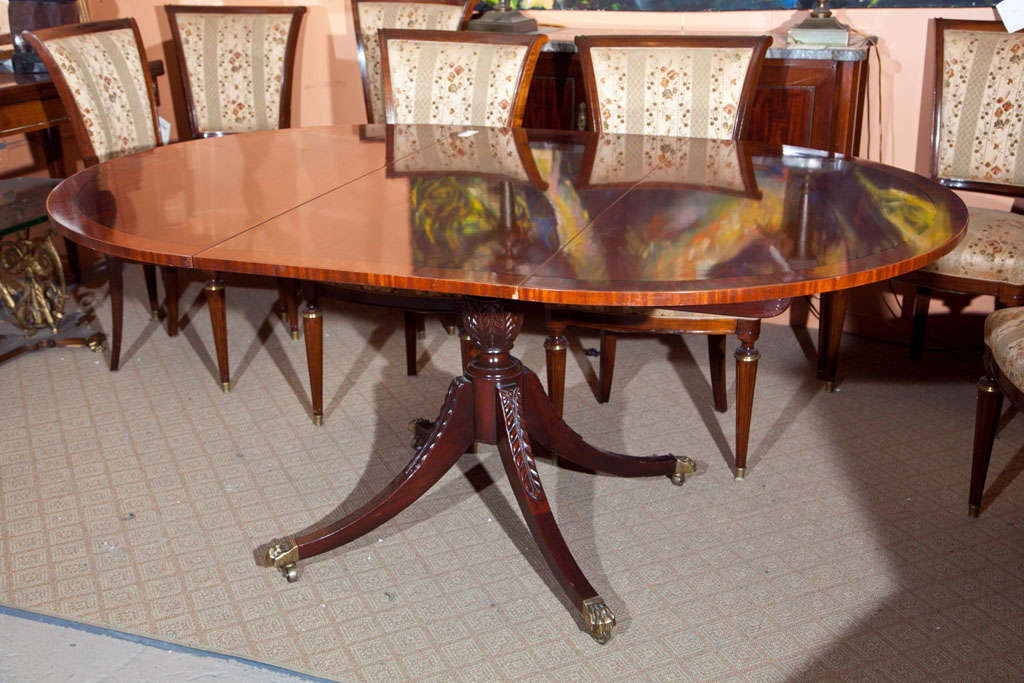 A custom quality circular dining table. The center quad legged pedestal on bronze casters supporting a great flame mahogany two leaf circular tabletop. The top polished. Possibly Baker. Two leaves each 21