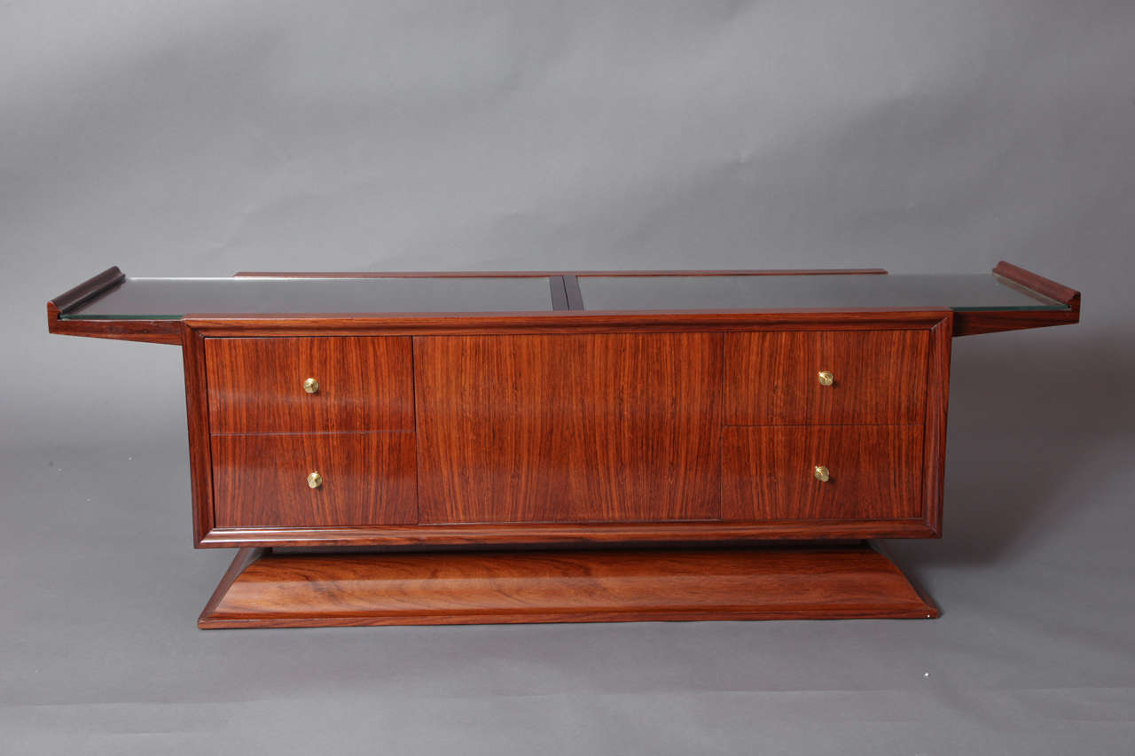 France, 1930s
Coffee table in polished wood, opens up to reveal concealed central bar cabinet, four drawers, interior in sycamore, bronze drawer pulls, inset glass panels protect top.
The table is fully finished on all sides.
55 x 16 x 17.5 H.