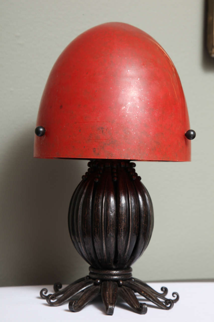 Louis Katona
lampe en fer et verre avec un pied ovoïde nervuré, des éléments ajourés, supportant un abat-jour en verre rouge chiné, années 1930.