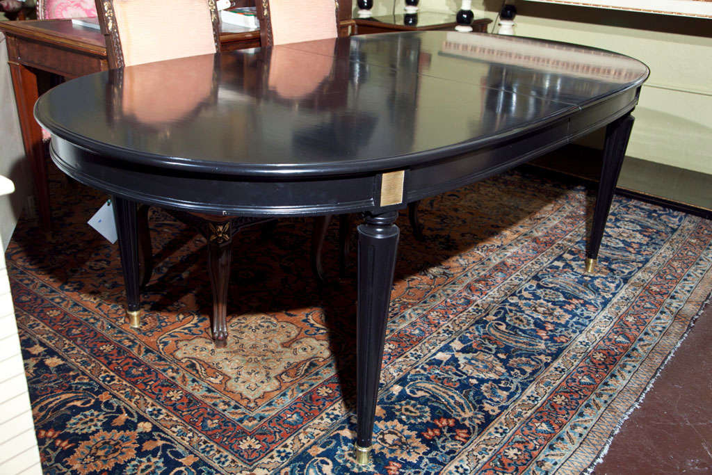 A fine Maison Jansen two-leaf dining room table. The capped bronze sabot feet leading to tapering Louis XVI style legs under a bronze-mounted apron supporting a solid ebonized top by Maison Jansen two 18 inch leaves.