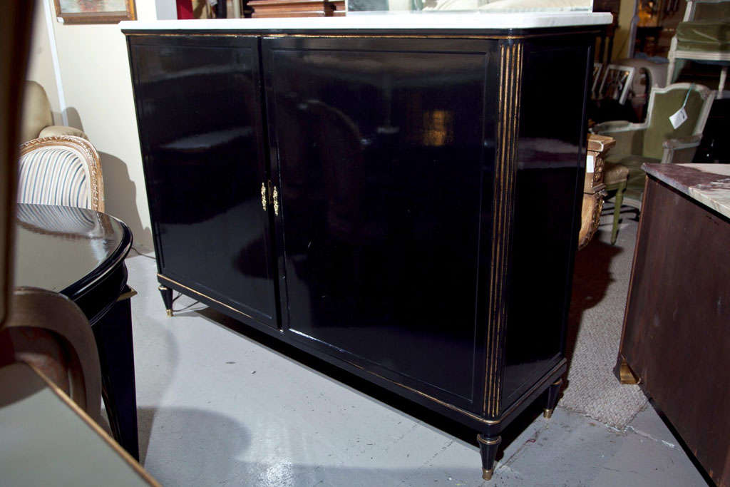 A gilt gold decorated ebonized two door cabinet - Armoire by Maison Jansen. The brass capped tappering legs supporting fluted gilt sides sitting under a white marble. The interior great to hang clothes or hide a flat screen TV.