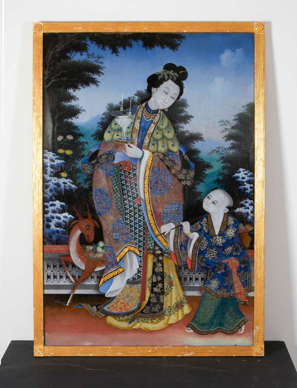 A very large and impressive Chinese reverse glass painting of a Maiden in court dress with an attendant, elaborately painted with fine brocade pattern and peacock feather cloak, holding a censer with a small deer to her left side. Mounted in gold